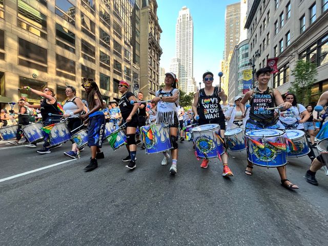 A line of women marching and playing drums